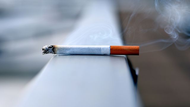 A lit cigarette resting on a ledge. 