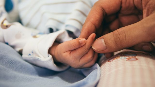 An adult holds a baby's hand.  