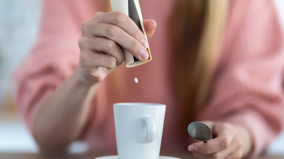 A woman puts a sweetener into a cup.