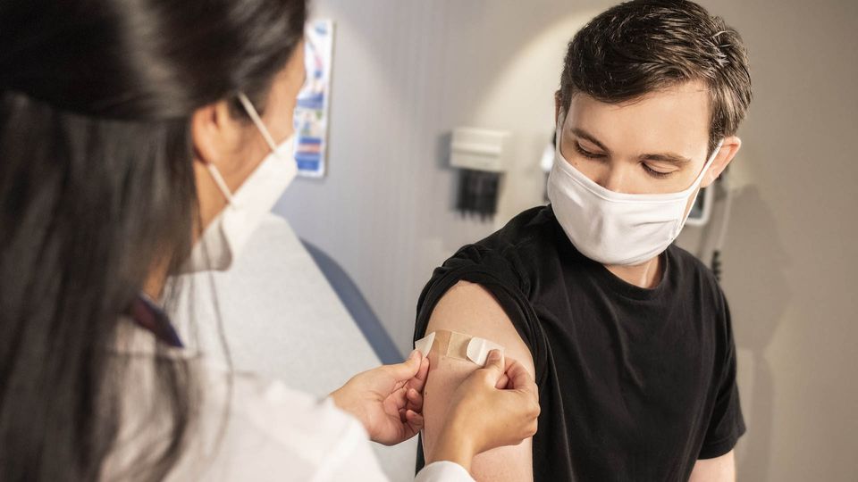 A health care provider placing a plaster on a patients arm after receiving a vaccine.