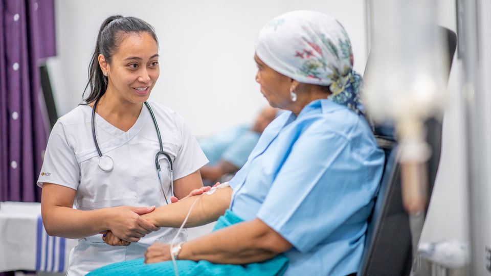 Cancer patient with a line in her arm talking to a medic with a stethoscope around her neck.