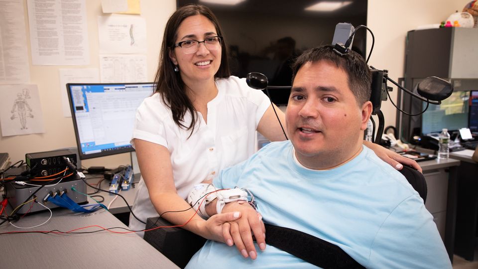 A woman and a woman hold hands. A device is embedded in the man's head.