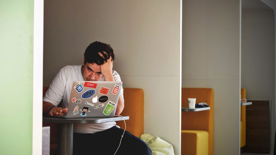 A man sitting at a table looking at a laptop with his hand in his hair.