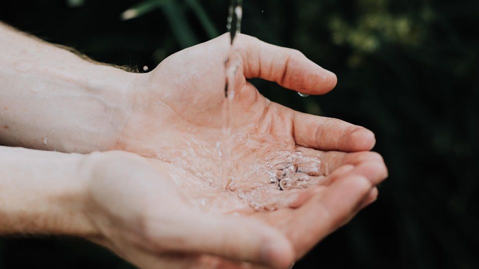 A person catches a stream of clean water in their cupped hands