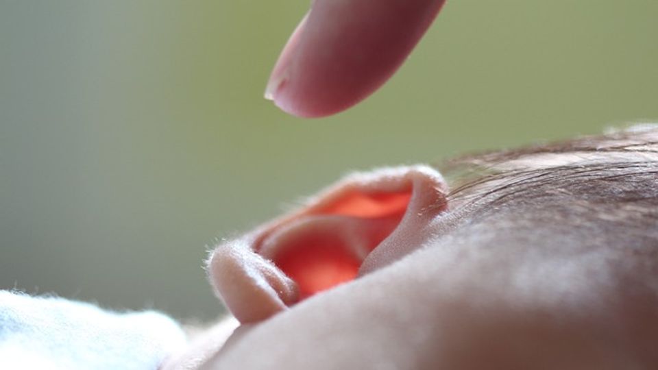 A finger reaching down to touch a young child's ear.