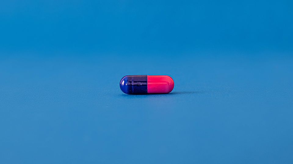 A dark blue and pink capsule against a blue background.