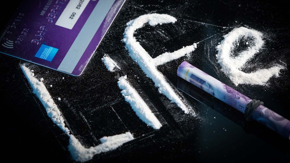 White powder spelling out the work 'Life' next to a bank card and a rolled bank note.