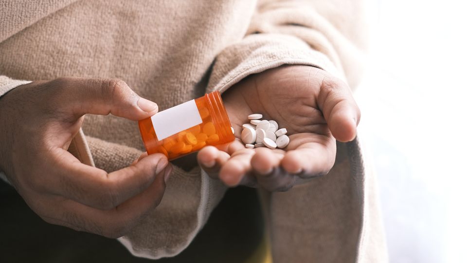 Someone pouring pills out into their hand from an orange pill bottle.