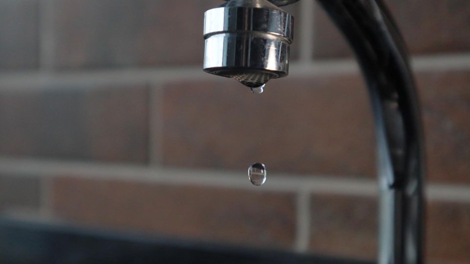 A droplet of water drips from a metal kitchen faucet.