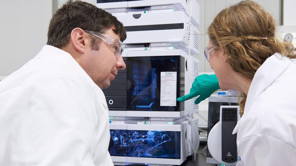 Two people in lab coats looking at an ACT label on a piece of analytical chemistry equipment.