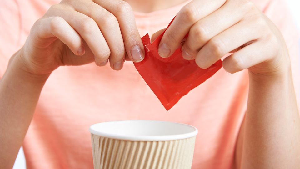 A person ripping open a packet of sweetener.
