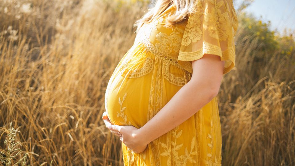 A pregnant woman in a yellow dress near some grass, representing how baby cells stay in the mother.