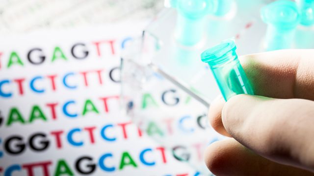 An individual holding a Eppendorf tube with paper reading DNA bases in the background. 