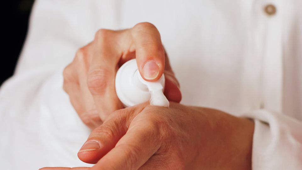 A person applying cream to their hand. 