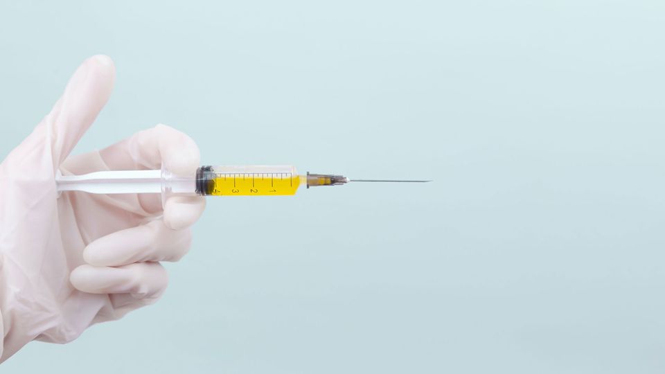 A gloved hand holds a syringe filled with yellow liquid.