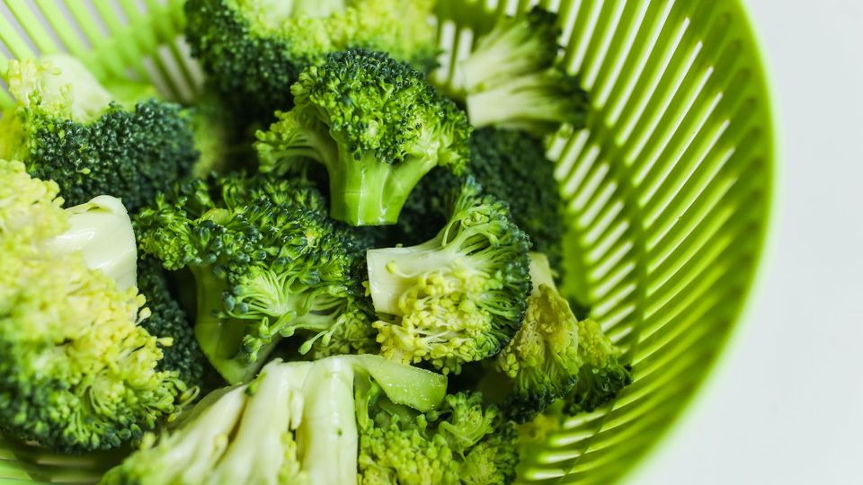 Broccoli florets in a green strainer.