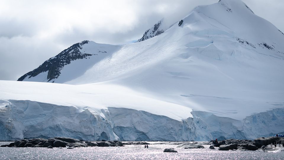 Two penguins in front of a large mountain in Antarctica.