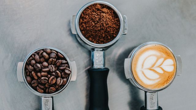 Three cups containing, coffee beans, ground up coffee, and a mug of coffee.