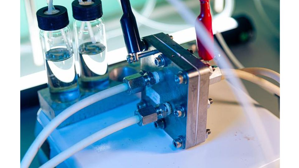 Two wires clipped to a sliver box with tubes coming off. Two vials of clear liquid sit to the side.
