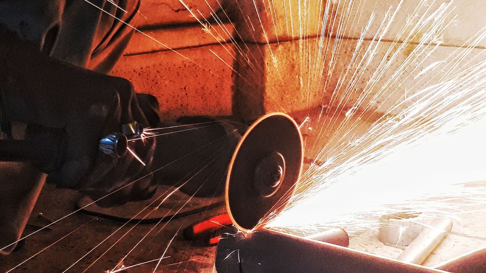 A person cutting into a steel pipe with an angle grinder, making sparks fly towards the viewer, representing a hardness test.