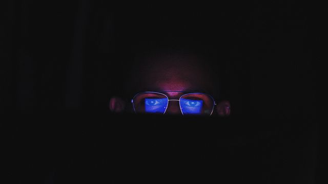 A man wearing glasses with the blue light from his device reflecting off them. 