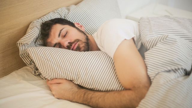 A man sleeps in a bed with stripy bed linen.