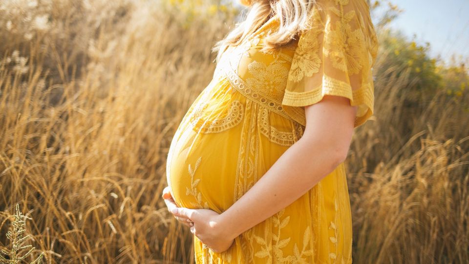 A pregnant woman in a yellow dress holds her belly.