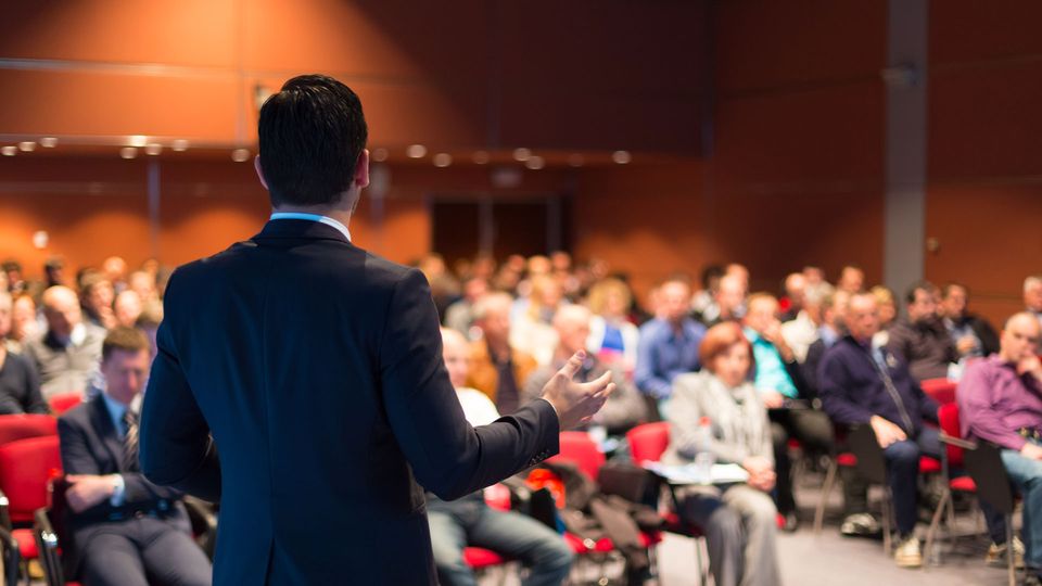 A speaker is presenting to a crowd at a conference