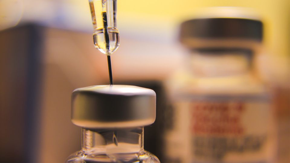 Close up of a syringe drawing liquid from a vial.