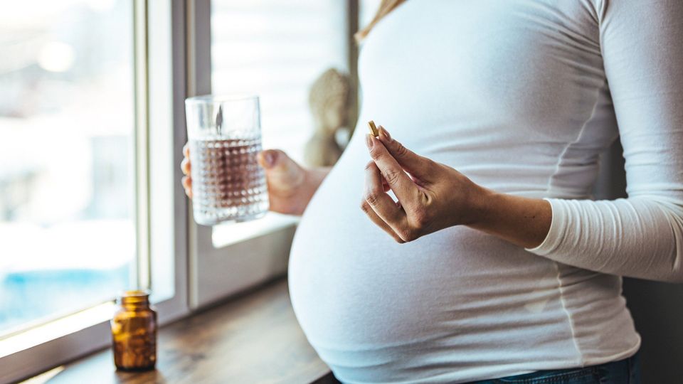 A pregnant woman talking a pill.