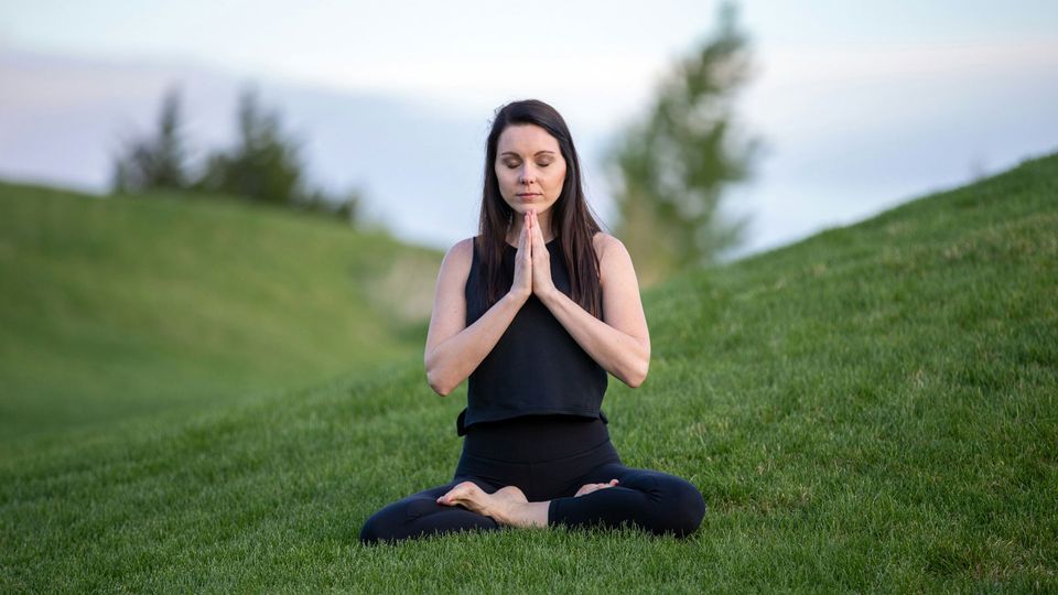 A woman sits cross-legged on grass.