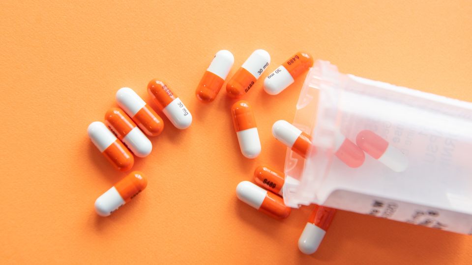 Orange and white capsules coming out of a plastic pill bottle.