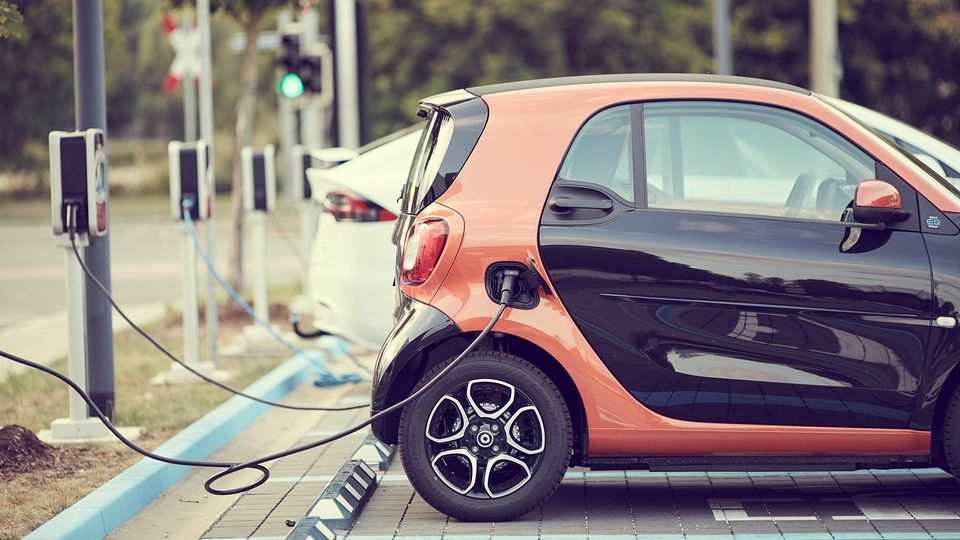 Orange and black electric car plugged into a charging point in a car park. 