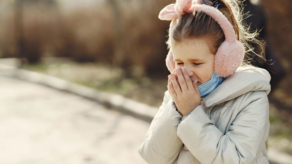 A child covers their mouth as they cough.