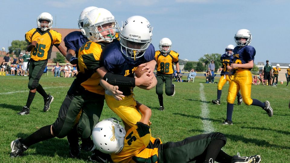 Children wearing helmets playing American football.