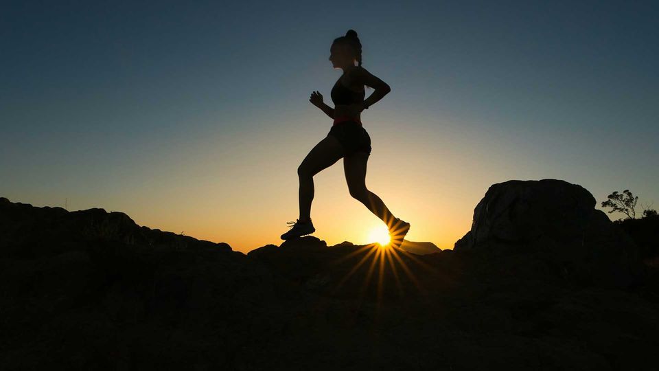 A woman running up a trail during sunset.