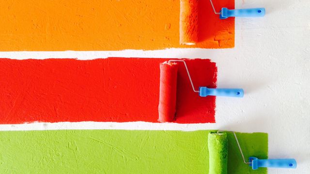 Three paint rollers painting strips of colour on a white wall. 