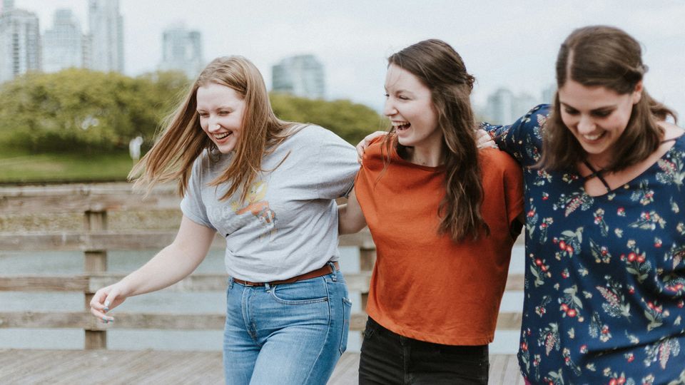 Three women with their arms round each other laughing.