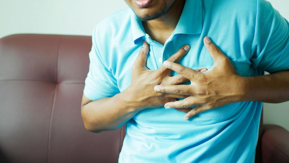 A man wearing a blue polo t shirt clutches his chest in pain.