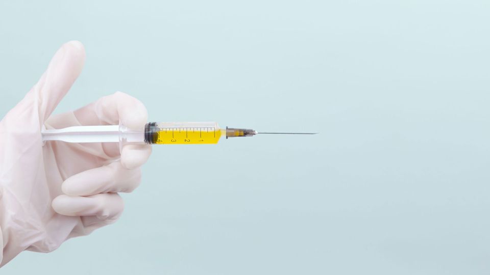 A gloved hand holds a syringe filled with yellow liquid.