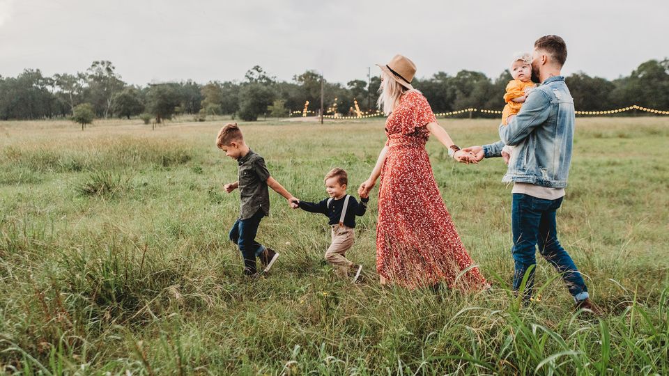 A family holding hands walking through a grass field.