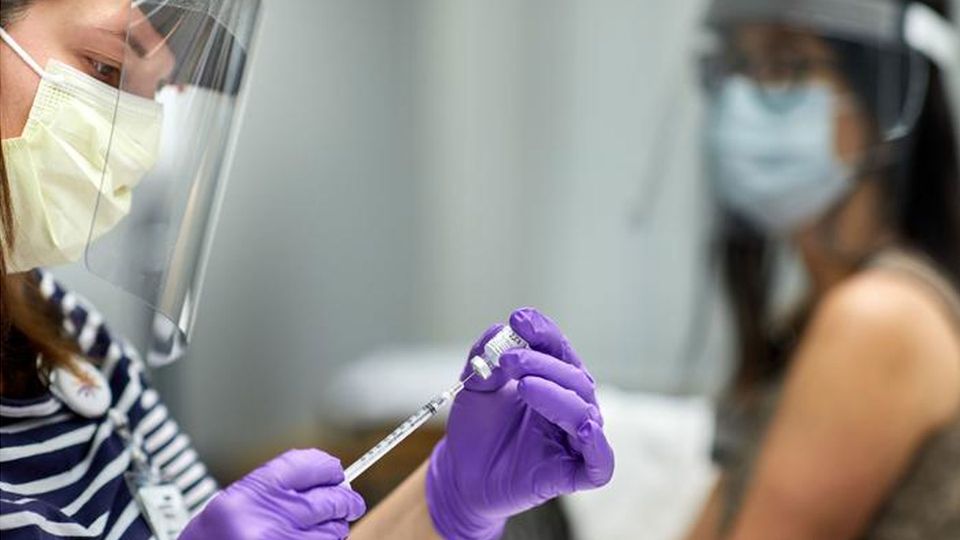 A healthcare worker wearing a visor and mask prepares a vaccine.