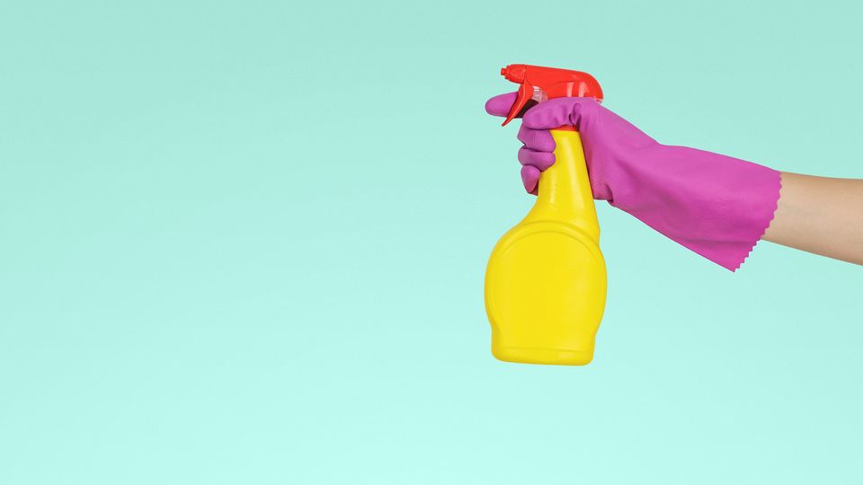 Someone holding a cleaning bottle with washing up gloves on.