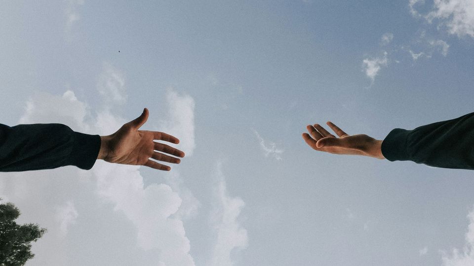Two hands reaching to each other against a blue sky.