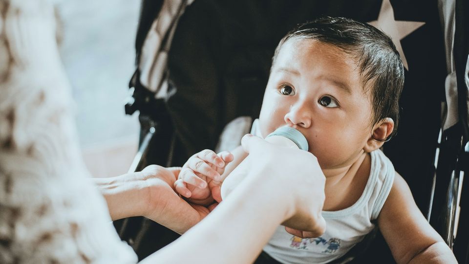 An infant drinks formula from a bottle.