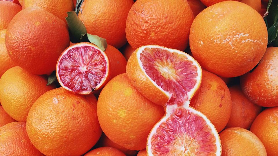 Two halved blood oranges lie on a pile of the fruit.