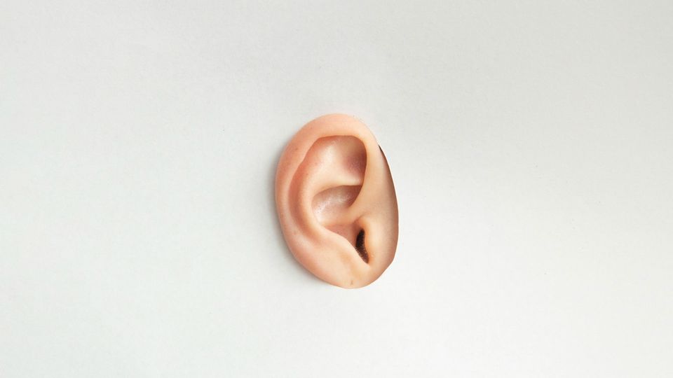 A person's ear poking through a hole in a piece of paper.
