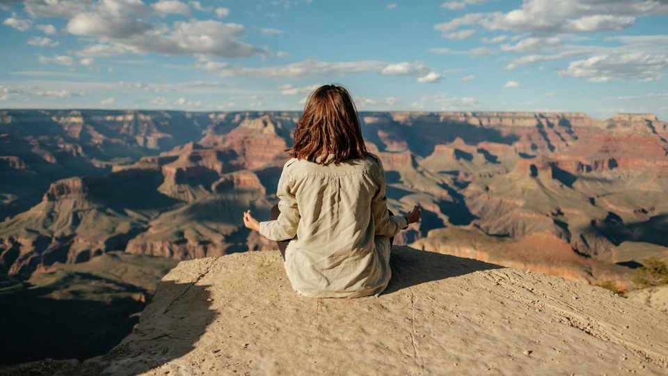 A woman meditates at the edge of a rocky cliff face
