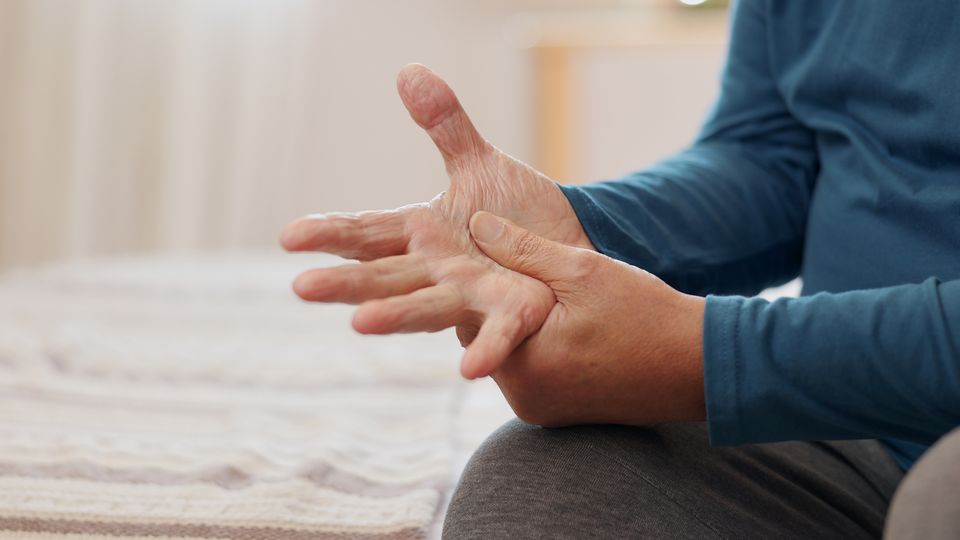 A man in a blue long-sleeve t-shirt rubs the palm of his right hand with his left thumb, as if to soothe some hand pain.