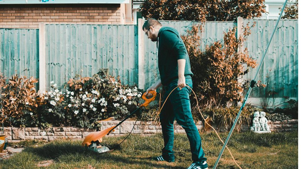 A man uses a strimmer on the lawn in a garden.